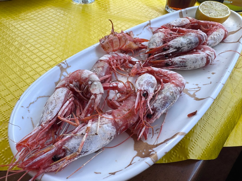 A platter of large, cooked shrimp arranged with a slice of lemon, set against a yellow tablecloth.